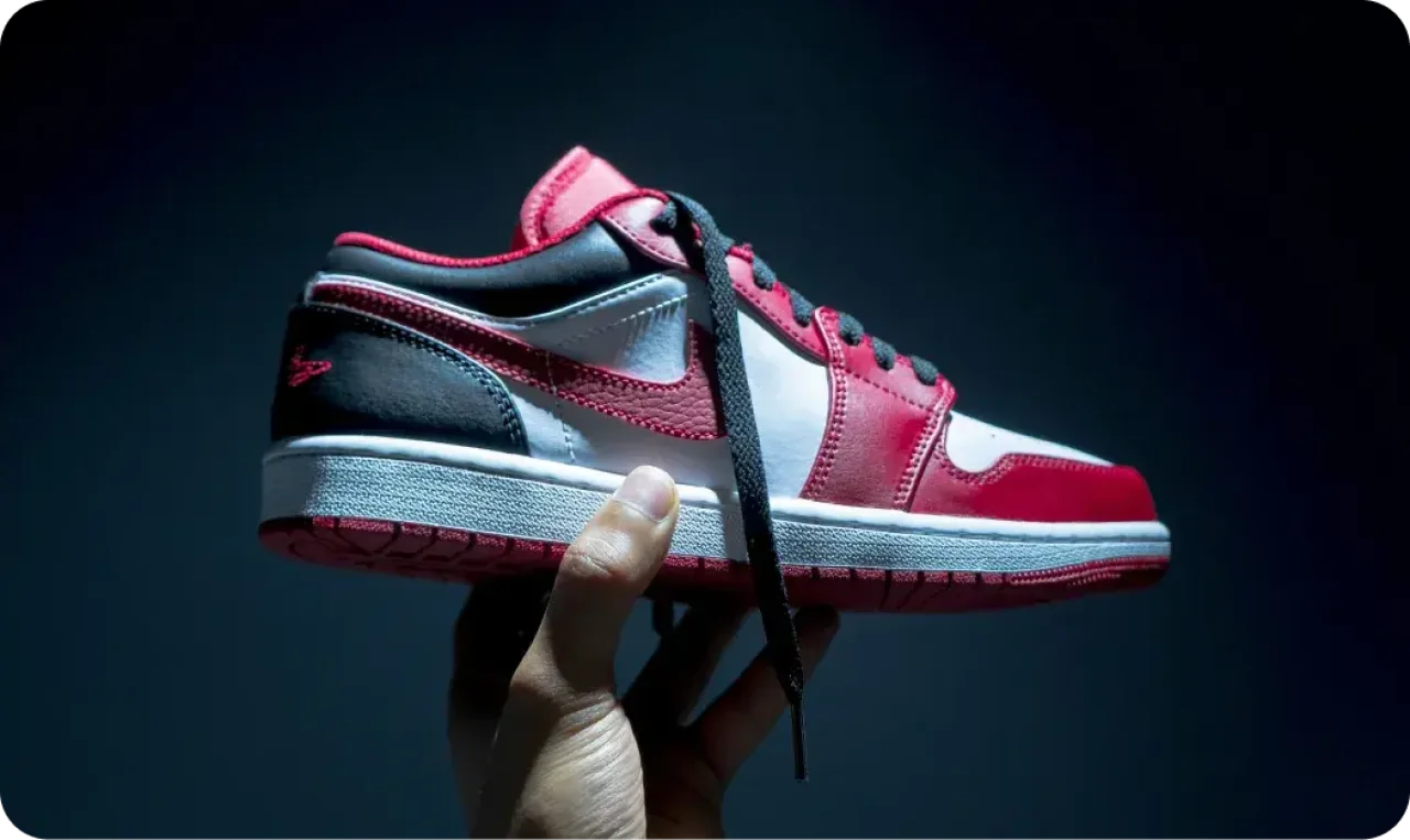 Hand Holding Red And White Sneaker In Dramatic Lighting