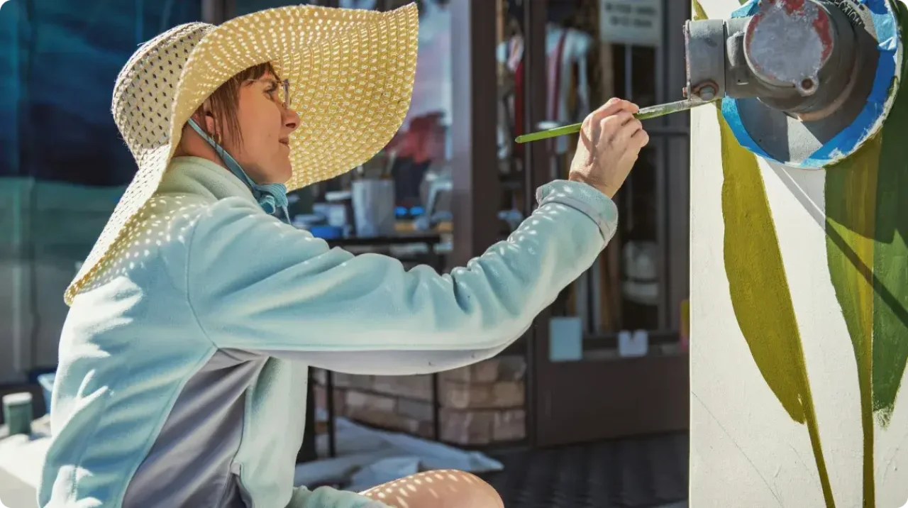 Woman Painting Mural Outdoors Wearing Sun Hat