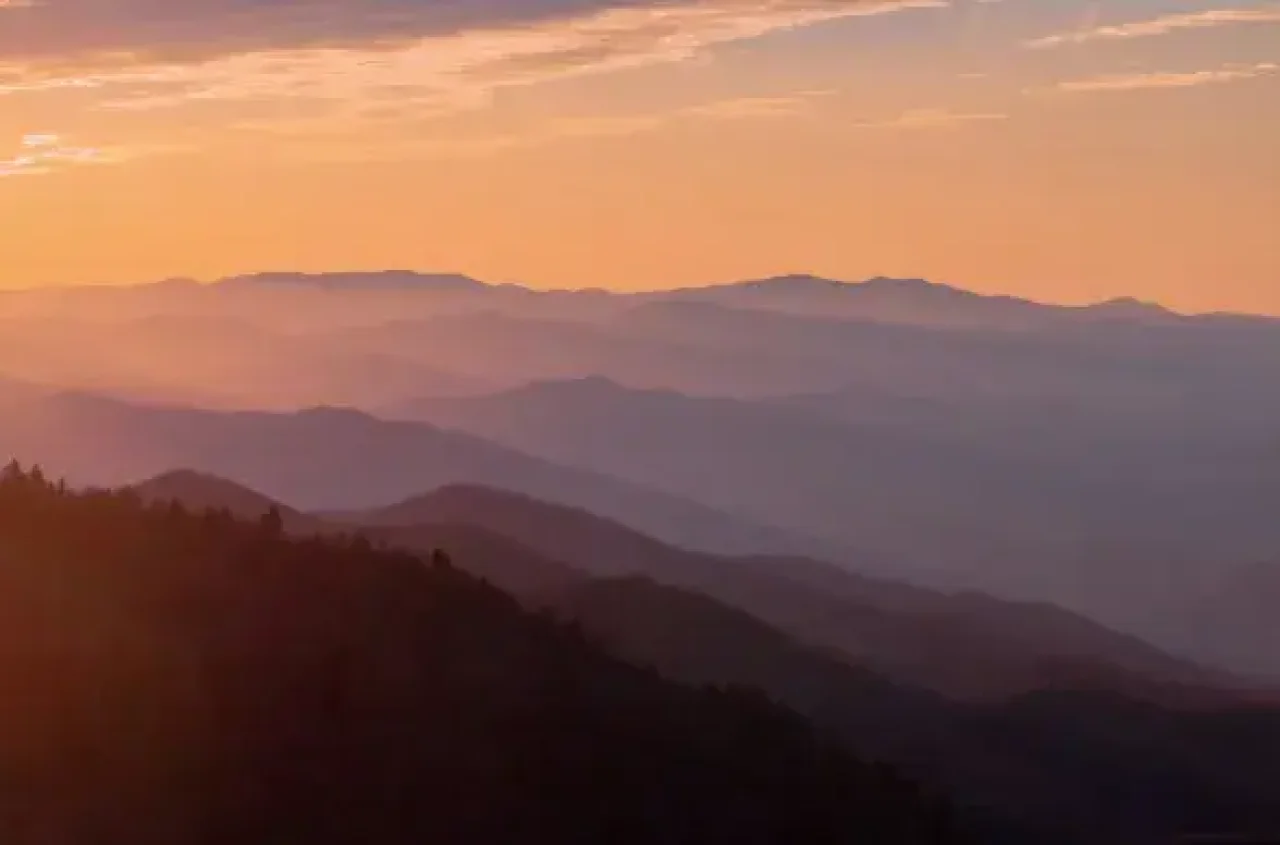 Layered mountain landscape with mist and an orange sunrise sky.