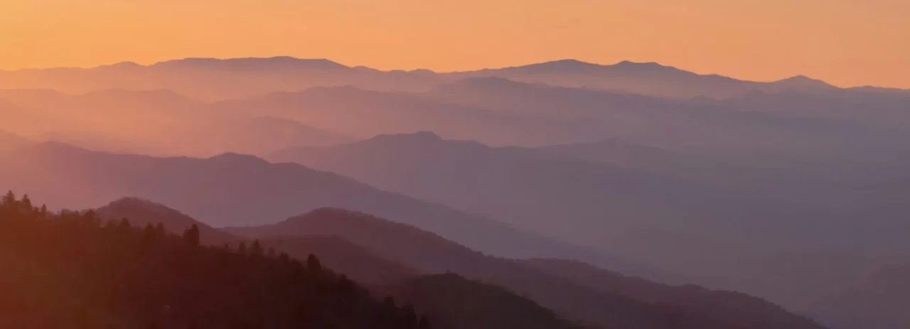 Layered mountain landscape with mist and an orange sunrise sky.