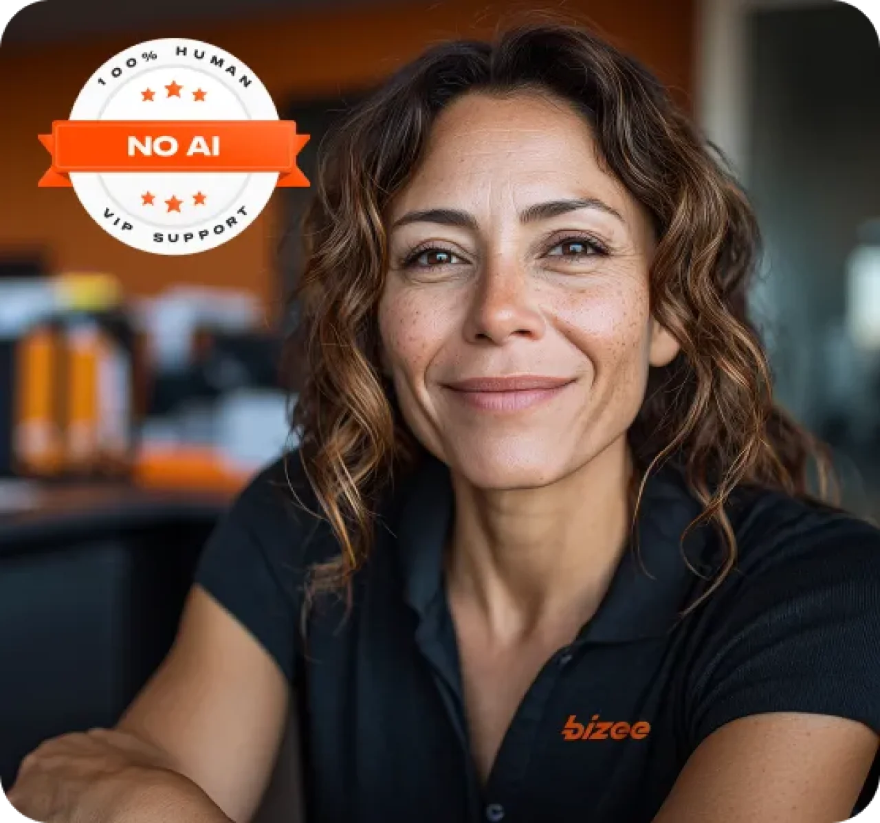 Bizee customer support agent smiling in office, wearing a black Bizee shirt, with a “100% Human, No AI, VIP Support” badge in the corner.